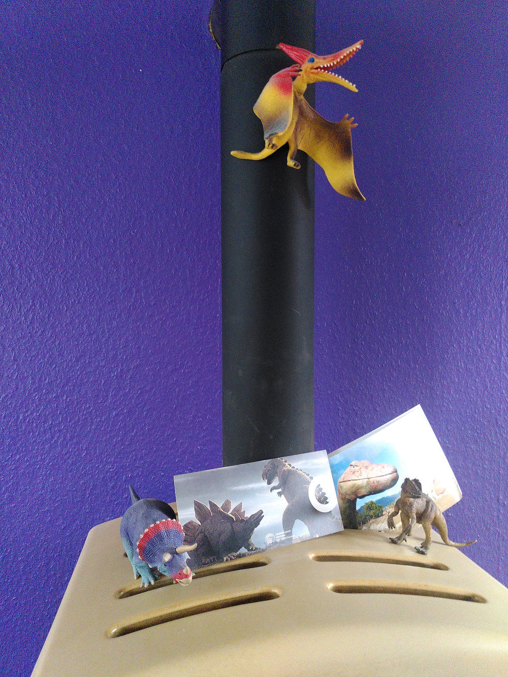 Farbfoto: von einem Ofen, auf dem zwei Saurierfiguren und zwei Postkarten mit Sauriern stehen, am Ofenrohr hängt eine bunte Flugsaurier-Figur.