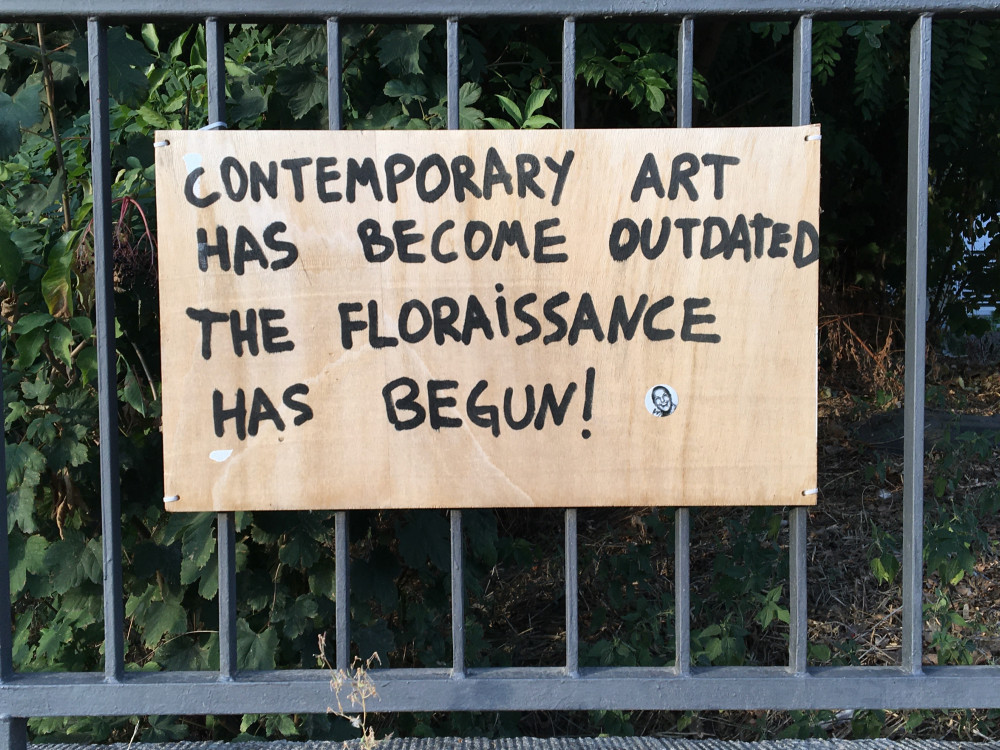 Abbildung zeigt ein handgeschriebenes Schild an einem Geländer am Rand der documenta fifteen mit der Aufschrift: „Contemporary Art has been become outdated. The Flouraissance has begun!“